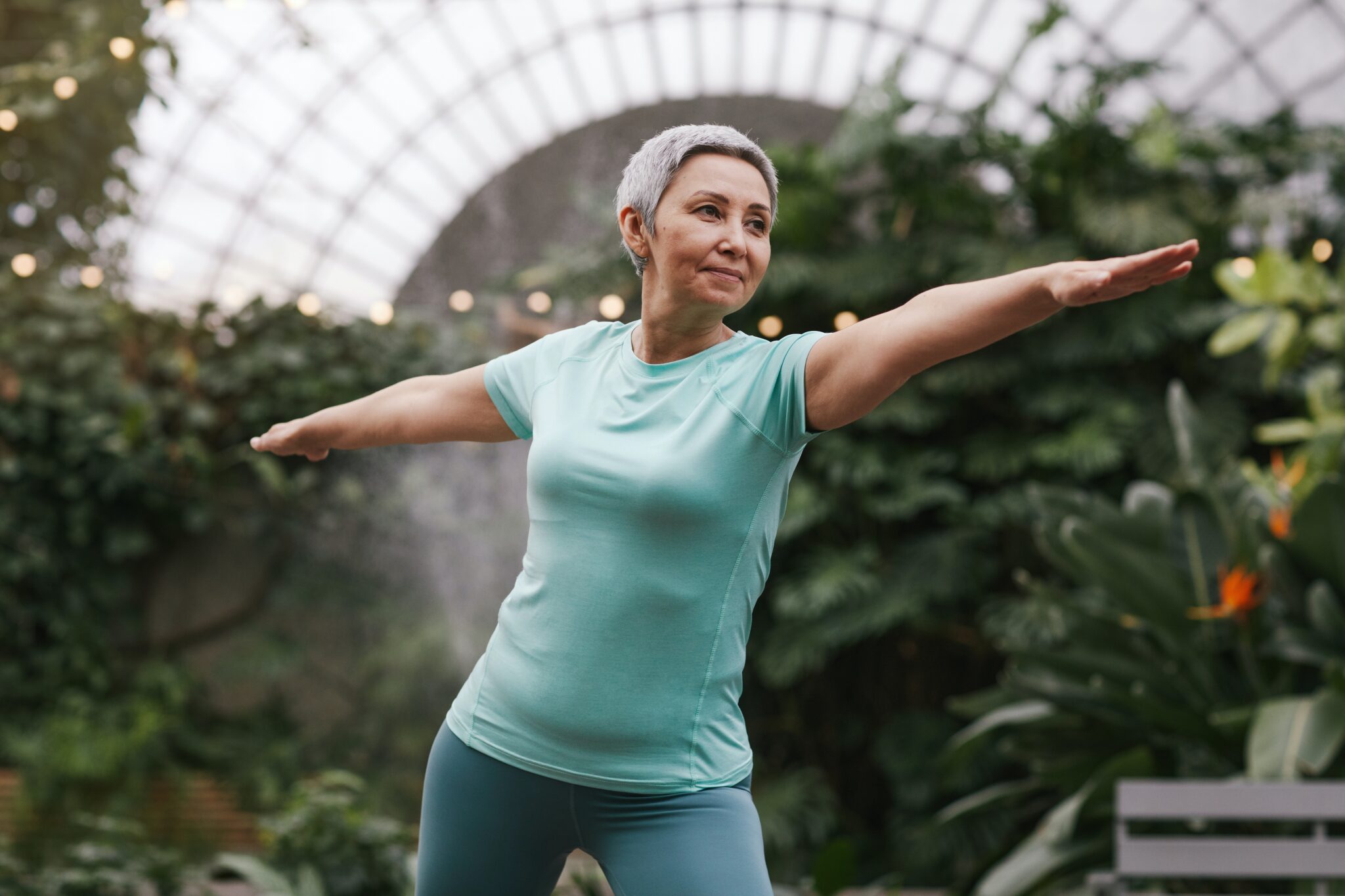 Old woman doing yoga with plants in the background